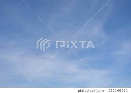Small aircraft flying high in a clear blue sky with soft clouds. A minimalistic outdoor scene highlighting aviation, open air and freedom of flight 133149321