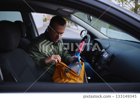 Man Organizes Gear Inside Car Cabin, Opens Yellow Backpack With Red Handle Equipment While Sitting Man Organizes Gear Inside Car Cabin, Opens Yellow Backpack With Red Handle Equipment While Sitting 133149345