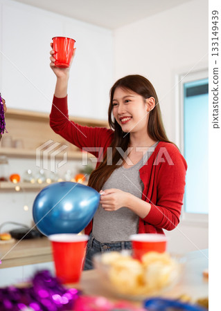 Party celebration. Young woman holding red cup and blue balloon at festive gathering. Party celebration. Young woman holding red cup and blue balloon at festive gathering. 133149439