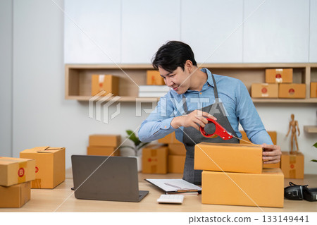 E-commerce. Young man sealing packages for shipment in a home office. 133149441