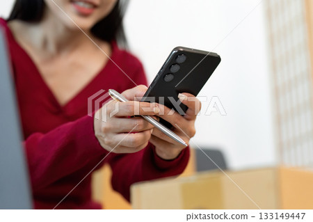 Remote Work: Woman Managing Deliveries with Smartphone and Pen 133149447