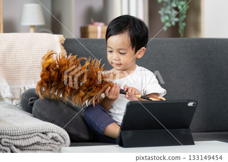 Child Playing with Tablet and Feather Duster in Cozy Living Room Child Playing with Tablet and Feather Duster in Cozy Living Room 133149454