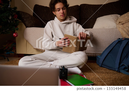 Teenage Boy in Hoodie Writing in Journal at Home During Christmas Season 133149458