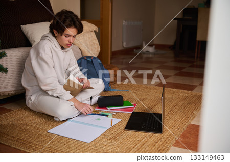 Teenage Boy Studying at Home With Laptop, Notebook, and Backpack 133149463