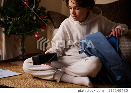 Teen Boy With Backpack At Home Checking Phone Near Christmas Tree For Modern Everyday Moment Teen Boy With Backpack At Home Checking Phone Near Christmas Tree For Modern Everyday Moment 133149480