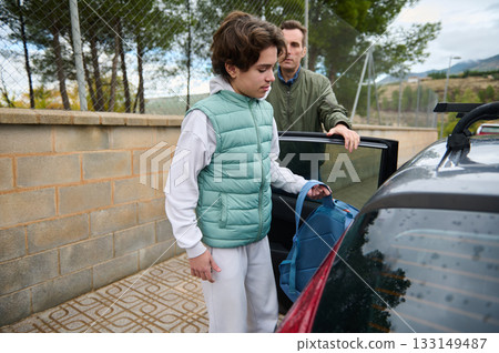 Teen Boy With Backpack Getting Into Car, Father Watches, Casual Family Moment On A Sunny Day 133149487