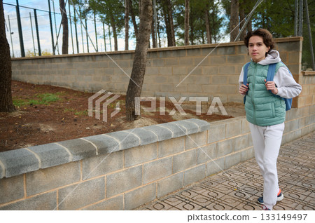 Teenage Boy With Backpack Walking Along Park Wall In Casual Winter Jacket Teenage Boy With Backpack Walking Along Park Wall In Casual Winter Jacket 133149497