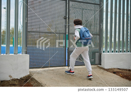 Teenager With Backpack Approaches Industrial Gate in Outdoor Fenced Area 133149507