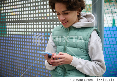 Teenage Boy With Smartphone At Outdoor Sports Court In A Green Puffer Vest Teenage Boy With Smartphone At Outdoor Sports Court In A Green Puffer Vest 133149513
