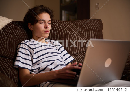 Teenage Boy Relaxing On Couch With Laptop And Game Controller At Home Teenage Boy Relaxing On Couch With Laptop And Game Controller At Home 133149542