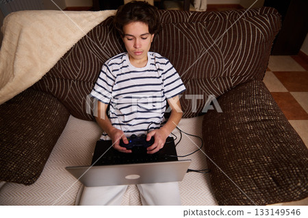 Teen Boy Playing Video Games on Laptop with Controller on Couch Teen Boy Playing Video Games on Laptop with Controller on Couch 133149546