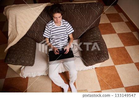 Teenage Boy Gaming On Laptop With Controller On Couch In Cozy Home Setting Teenage Boy Gaming On Laptop With Controller On Couch In Cozy Home Setting 133149547
