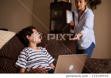 Teen Boy On Couch With Laptop As Mother Interacts At Home, A Warm Family Moment 133149554