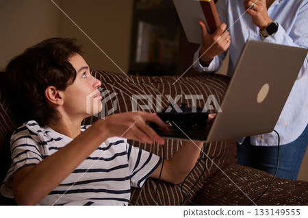 Teen Gamer Receives Help From Friend With Laptop In Cozy Living Room 133149555