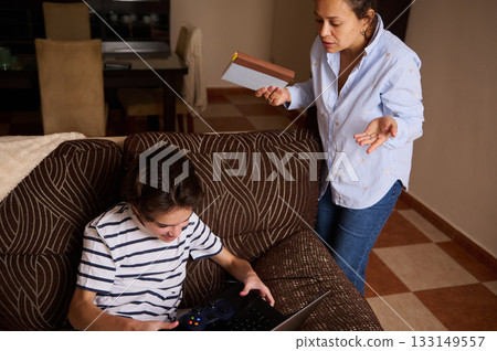 Mother Helps Teen Boy With Laptop and Game Controller in Cozy Living Room Scene Mother Helps Teen Boy With Laptop and Game Controller in Cozy Living Room Scene 133149557