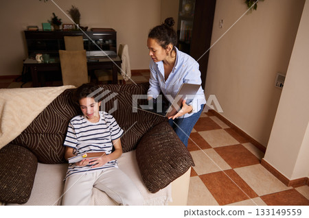 Mother Helps Teen Boy With Homework At Home, Laptop Open In Cozy Living Room Mother Helps Teen Boy With Homework At Home, Laptop Open In Cozy Living Room 133149559