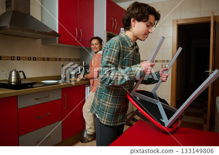 Teen Boy Assembling Chair in Modern Kitchen, Family Moment, Home Life, Happy Atmosphere Teen Boy Assembling Chair in Modern Kitchen, Family Moment, Home Life, Happy Atmosphere 133149806