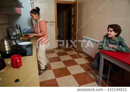 Teenage Boy Converses With Friend While Woman Cooks in Bright Modern Kitchen At Home Today Teenage Boy Converses With Friend While Woman Cooks in Bright Modern Kitchen At Home Today 133149812