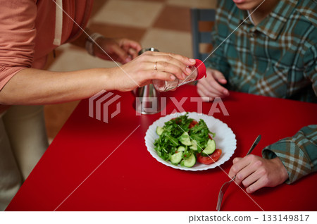 Teenage Friends Sharing Salad at Red Table While Salt Is Shaken Onto Plate Teenage Friends Sharing Salad at Red Table While Salt Is Shaken Onto Plate 133149817