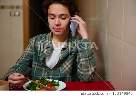 Teenage Boy Eating Salad While Talking on Phone in Plaid Shirt at Diner 133149843