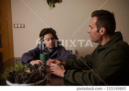 Teenager And Father Share Conversation Over Mugs At Cozy Kitchen Table Teenager And Father Share Conversation Over Mugs At Cozy Kitchen Table 133149865