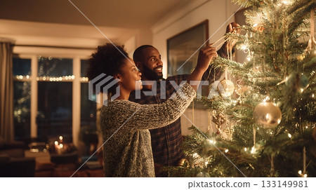 Smiling couple decorating Christmas tree together. Holiday lights, baubles and cozy atmosphere for Christmas and New Year season 133149981