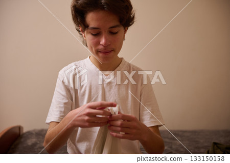 Teenage Boy Unpacking On Bed, Quiet Focus And Curiosity At Home In A Simple White Tee Teenage Boy Unpacking On Bed, Quiet Focus And Curiosity At Home In A Simple White Tee 133150158