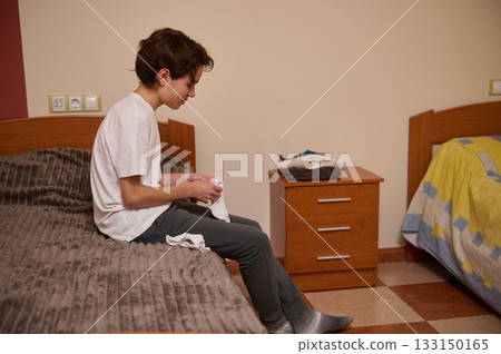 Teen Boy Folding Laundry In Bedroom During A Quiet Home Morning 133150165