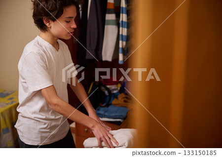 Teenage Boy Folding Laundry In A Closet Bedroom Scene During A Quiet Morning At Home 133150185