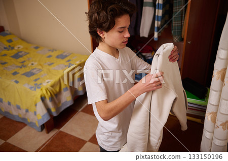 Teenage Boy Organizes Clothes In Bedroom, Preparing Outfit For Day Teenage Boy Organizes Clothes In Bedroom, Preparing Outfit For Day 133150196