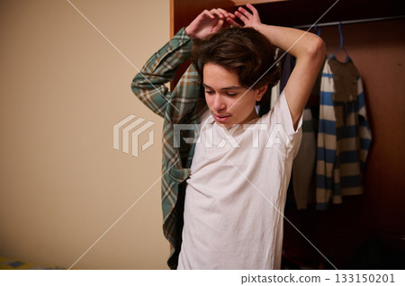 Teenager Adjusting His Shirt In A Bedroom Closet, Casual Indoor Moment Of Self Expression 133150201