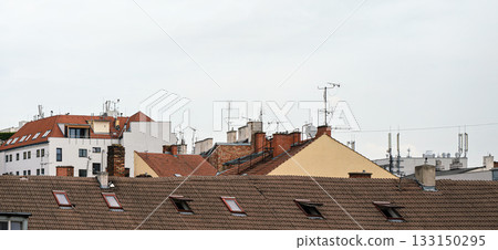 Building roofs with many tv and internet antennas, some satellite dishes, overcast sky above 133150295