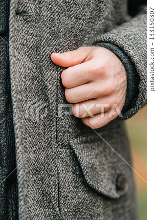 Textured herringbone overcoat detail with wood button and human hand gesture. Textured herringbone overcoat detail with wood button and human hand gesture. 133150307