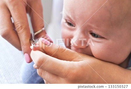 Infant baby boy having his nails cut by mother, detail on scissors and fingertips 133150327