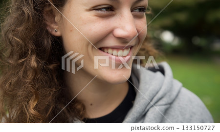 Happy young woman with curly hair and natural skin texture smiling outdoors. Confidence and real beauty representation. Acne positivity movement 133150727