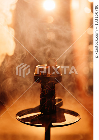 Hookah bowl with glowing coal and drifting smoke in warm bokeh bar light Hookah bowl with glowing coal and drifting smoke in warm bokeh bar light 133150780