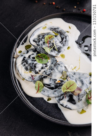 Black ravioli in creamy white sauce with microgreens, gourmet plating on dark slate Black ravioli in creamy white sauce with microgreens, gourmet plating on dark slate 133150781
