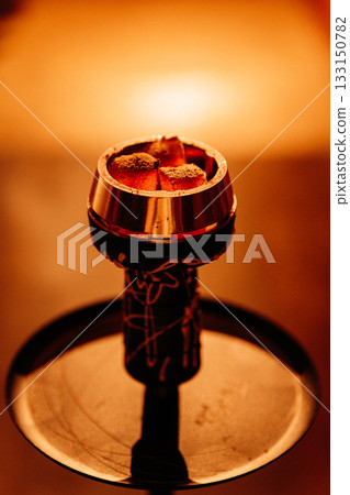 Glowing hookah coals in a metal bowl, warm bokeh bar lighting, macro closeup 133150782