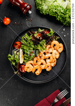 Grilled shrimp salad with mixed greens, cherry tomatoes and lemon on a black plate Grilled shrimp salad with mixed greens, cherry tomatoes and lemon on a black plate 133150784