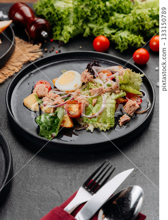 Tuna salad with egg, tomatoes and greens on black plate, restaurant lunch closeup Tuna salad with egg, tomatoes and greens on black plate, restaurant lunch closeup 133150789