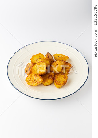 Golden roasted potato chunks on a plate, crispy and seasoned, isolated on white 133150796