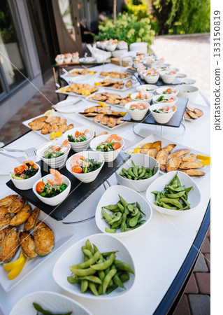 Catering buffet with edamame bowls, shrimp salads, and baked mussels outdoors 133150819