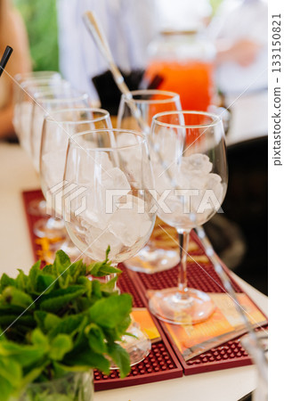 Wine glasses packed with ice and fresh mint on a bar, cocktail prep at a summer event Wine glasses packed with ice and fresh mint on a bar, cocktail prep at a summer event 133150821
