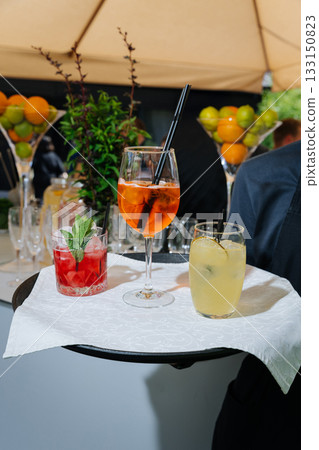 Waiter tray with Aperol Spritz, berry cocktail and lemonade at an outdoor event 133150823