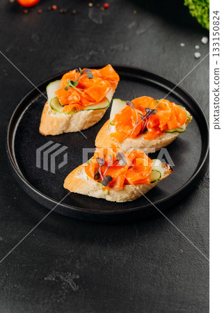 Salmon canapes on baguette with cucumber and cream cheese on black plate 133150824