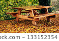 Wooden picnic table in autumn park surrounded by fallen yellow leaves 133152354