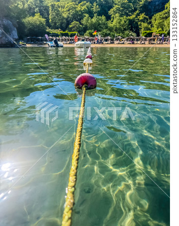 close-up view of a rope line with red and white safety buoys floating in crystal-clear seawater, with a sandy beach and green forest in the background. High quality photo close-up view of a rope line with red and white safety buoys floating in crystal-clear seawater, with a sandy beach and green forest in the background. High quality photo 133152864