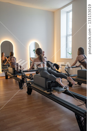 Fitness instructors performing pilates exercises using reformer beds and resistance bands, promoting healthy lifestyle and core strengthening 133153019