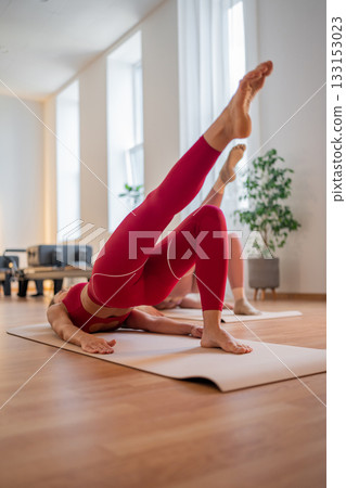 Pilates women performing inverted leg raises, pair of women practicing inverted leg raises with focus on the buttocks 133153023