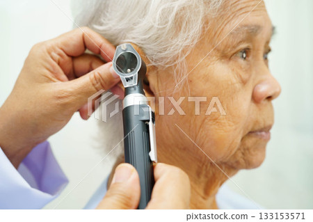 Otolaryngologist or ENT physician doctor examining senior patient ear with otoscope, hearing loss problem. 133153571